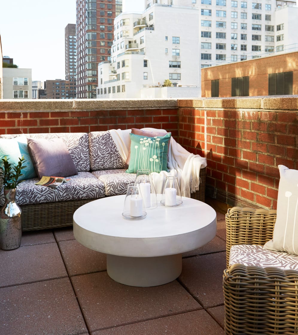 A couch and chair on the terrace of the Gardens Suite Hotel. A large round coffee table holds three candles encased in a clear glass. New York City skyscrapers can be seen behind.