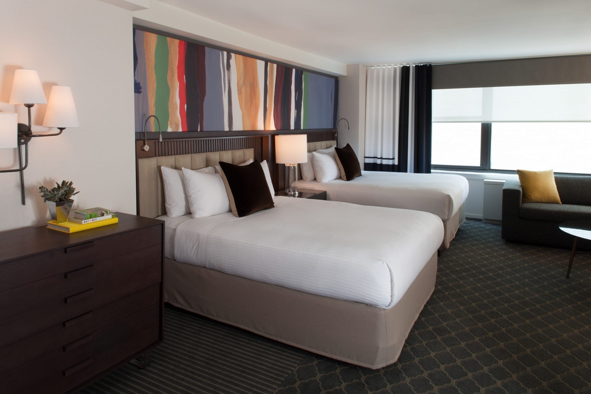 Perspective view of two queen beds inside the Junior Suite of Fifty Hotel. A wide canvas of artwork is hung above.