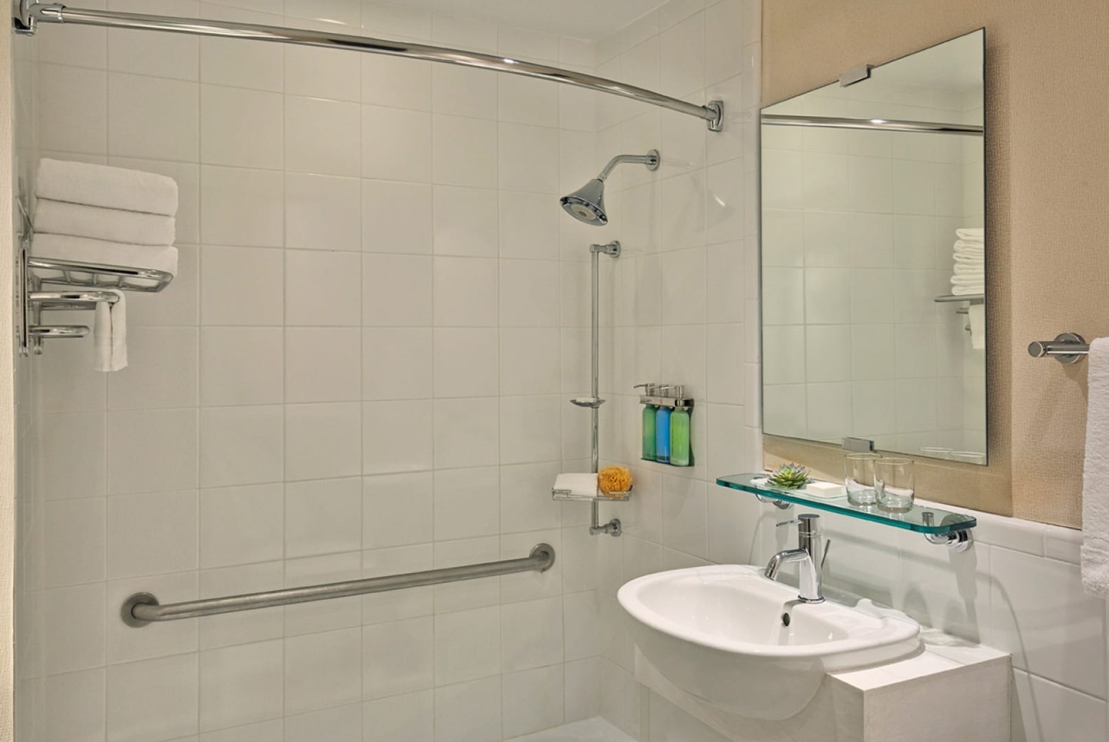 View to the shower inside an Affinia Gardens Suites bathroom. To one side is a sink, with rectangle mirror above it.