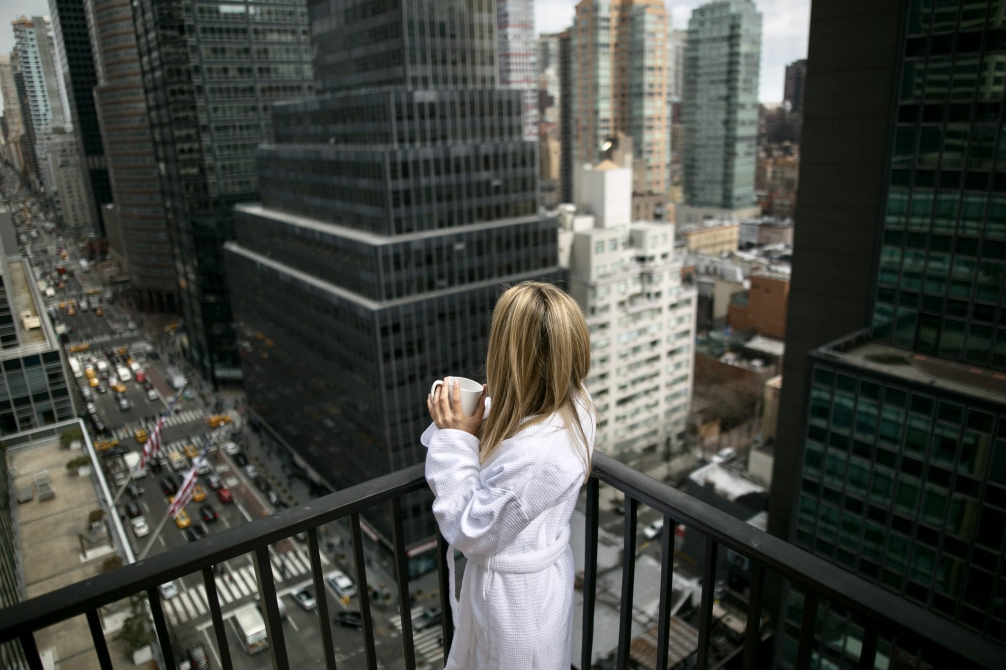 Overhead shot of a blonde person standing at the corner of the balcony railing. Affinia 50 offers views of the city from your room and the terraces.